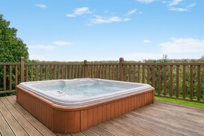Een hottub op een houten terras, met een houten hek en begroeiing op de achtergrond.