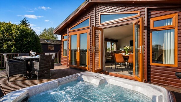 A wooden cabin with a hot tub, outdoor dining area, and sliding glass doors leading to a living room. - 2 Bed in Athelington (oc-h35081) (Athelington)