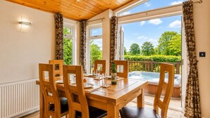 A wooden dining table with chairs, a hot tub, and a view of greenery outside. - 2 Bed in Athelington (oc-h35081) (Athelington)