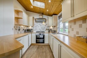 A modern kitchen with white cabinets, a wooden countertop, a built-in oven, and a window providing a view outside. - 2 Bed in Athelington (oc-s35083) (Athelington)