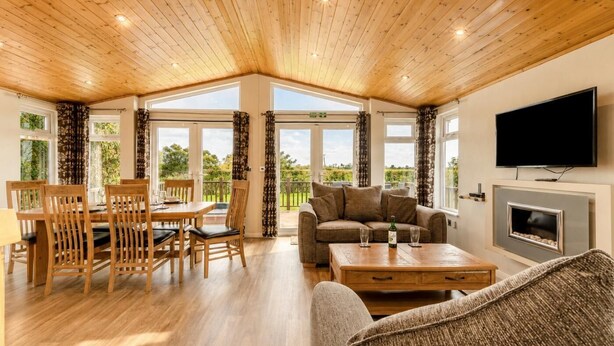 Une pièce spacieuse avec un plafond en bois, un coin repas comprenant des chaises et une table en bois, un canapé, un téléviseur à écran plat et une cheminée.