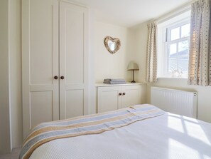 Ein Schlafzimmer mit Bett, Kleiderschrank, Kommode, Spiegel, Lampe und einem Fenster mit Vorhängen.