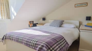Un dormitorio con cama, mesita de noche, lámpara, un cuadro en la pared y una ventana con cortinas.