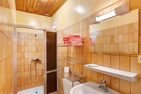 A bathroom with a shower, toilet, sink, and a towel rack with towels.