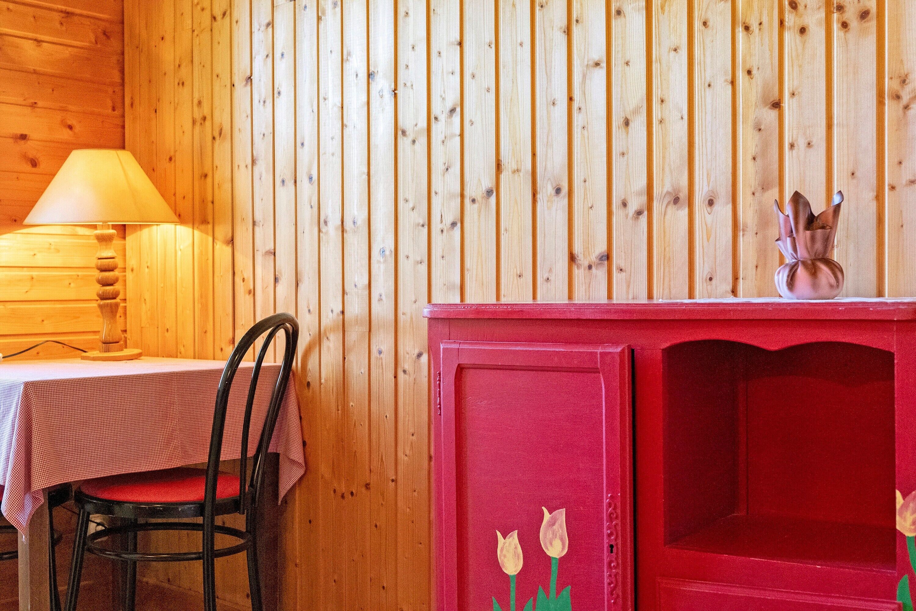 Un intérieur en bois avec une table et une chaise, une lampe et un buffet rouge orné de motifs floraux.