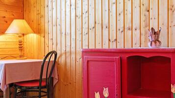 Un intérieur en bois avec une table et une chaise, une lampe et un buffet rouge orné de motifs floraux.