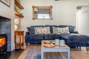 Ein Wohnzimmer mit einem dunkelblauen Sofa, einem Kamin, einem Couchtisch mit Dekoration und einem hölzernen Spiegel an der Wand.