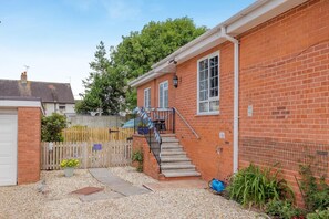 A red brick house with a white garage door, a wooden fence, and a gravel driveway. - 1 Bed in Woodbury (oc-w37536) (Woodbury)