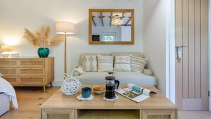 Una sala de estar acogedora con techo de madera, un sofá con cojines estampados, una mesa de centro con varios objetos y una puerta de madera.