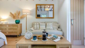 A cozy living room with a wooden ceiling, a sofa with patterned cushions, a coffee table with various items, and a wooden door.
