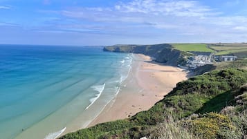 A coastal landscape with a sandy beach, cliffs, and a building complex.