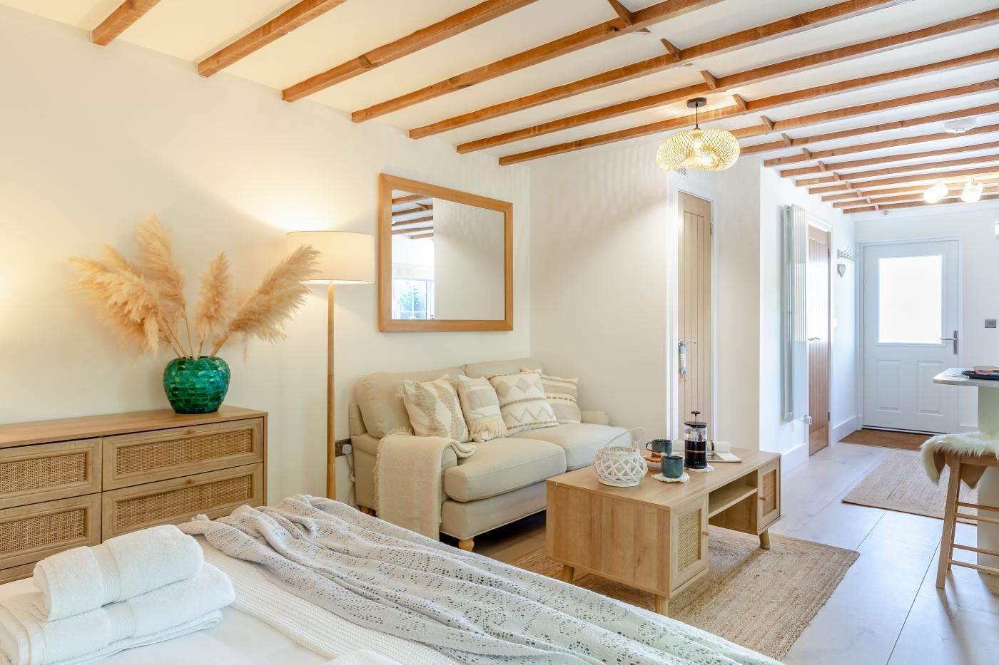 A cozy bedroom with a bed, a sofa, a wooden dresser, a mirror, and a lamp.