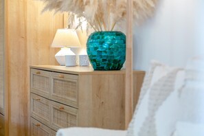 A wooden nightstand with a white lamp and a decorative teal vase.