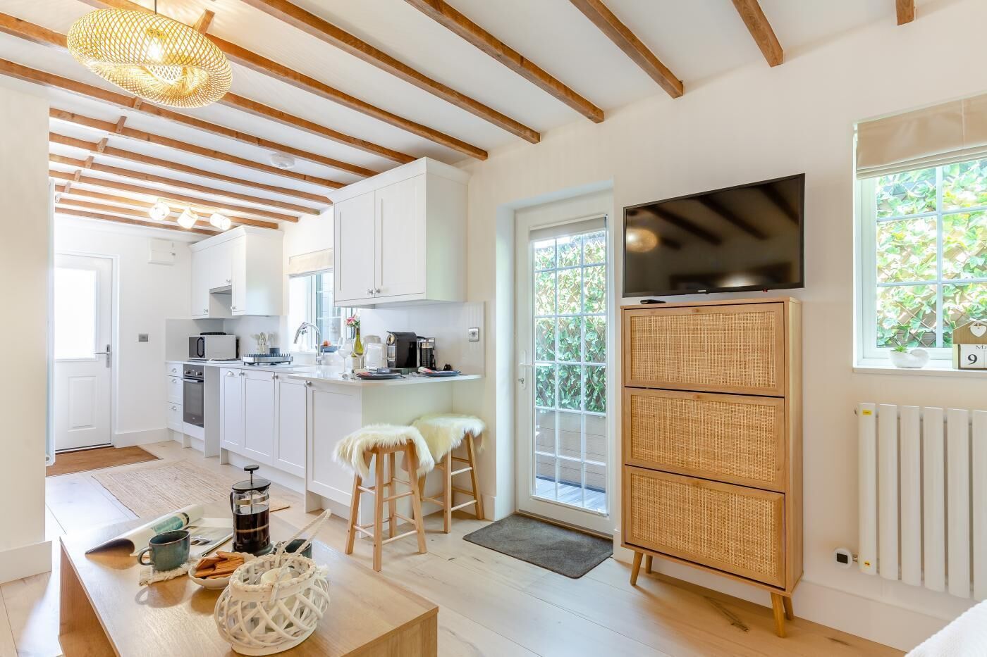A modern kitchen with white cabinets, a dining area with stools, a TV, and a large window.