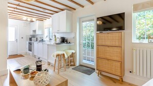 Una cocina moderna con armarios blancos, una zona de comedor con taburetes, un televisor y un ventanal grande.