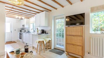 A modern kitchen with white cabinets, a dining area with stools, a TV, and a large window.