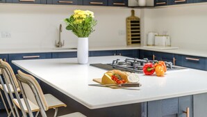 Une cuisine moderne avec des meubles de couleur sombre, un plan de travail blanc, une cuisinière à gaz et un vase rempli de fleurs.