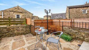 Un bâtiment en pierre avec une clôture en bois, une petite table avec des chaises et un lampadaire.