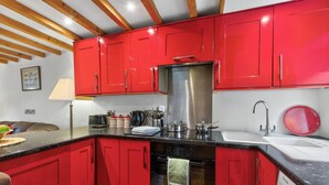 Une cuisine avec des meubles de rangement rouges, une hotte de cuisinière en acier inoxydable, un lave-vaisselle et un évier.