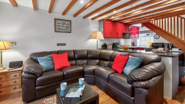 Un salon moderne avec un canapé d’angle en cuir, une petite table basse et un coin cuisine doté de meubles rouges.