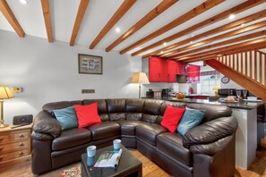 A modern living room with a leather sectional sofa, a small coffee table, and a kitchen area with red cabinets. - 1 Bed in Askrigg (oc-s39029) (Askrigg)