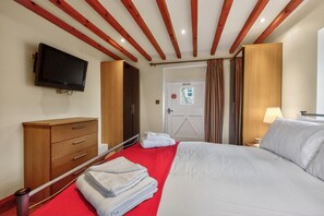 Ein Hotelzimmer mit einem Bett, einem an der Wand montierten Fernseher, einer Holzkommode, einem Kleiderschrank und einer Tür mit Fenster.
