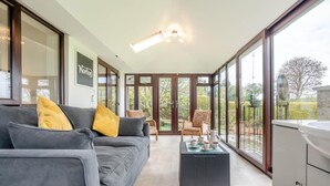 Ein modernes Wohnzimmer mit grauem Sofa, gelben Kissen, einem Couchtisch und Blick ins Freie durch große Fenster.