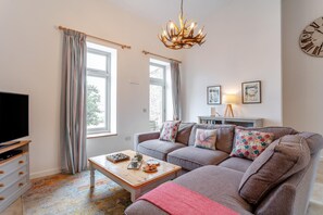 A living room with a sofa, coffee table, television, and a chandelier. - 1 Bed in Pennymoor (oc-s39043) (Pennymoor)