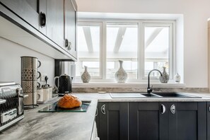 Une cuisine avec un plan de travail en marbre, une miche de pain, une machine à café et des vases décoratifs sur le rebord de la fenêtre.