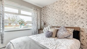 Une chambre à coucher avec un lit, une fenêtre avec des rideaux, un radiateur et un papier peint à motifs floraux.