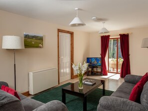 A living room with a sofa, a coffee table, a lamp, a TV, and a painting on the wall. - 4 Bed in Llandovery (oc-bn208) (Llanfair-ar-y-Bryn)