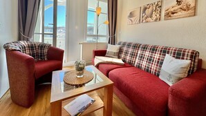 Una sala de estar acogedora con un sofá rojo, un sillón rojo, una mesa de centro de vidrio y vistas de la ciudad a través de amplios ventanales.