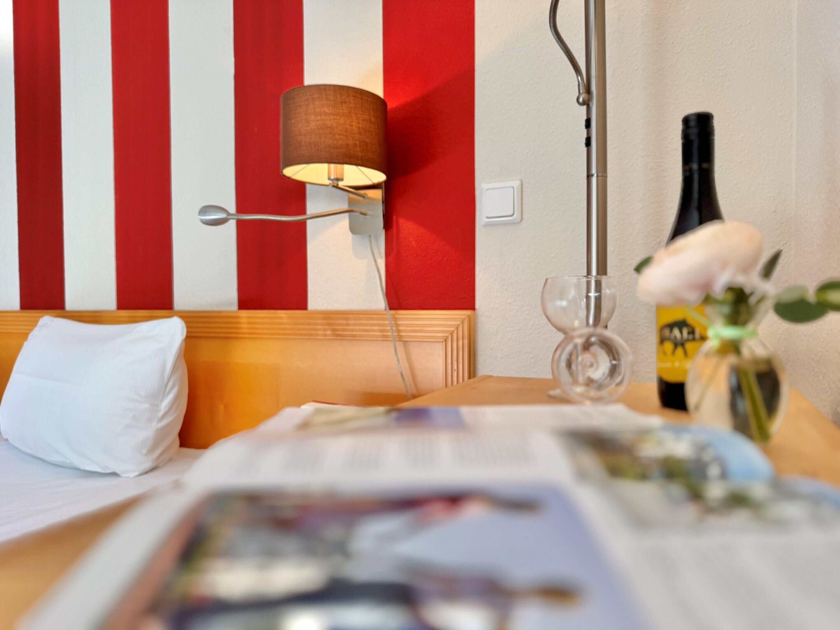Et hotelværelse med en seng, en senget lampe, en flaske og en vase med blomster.
