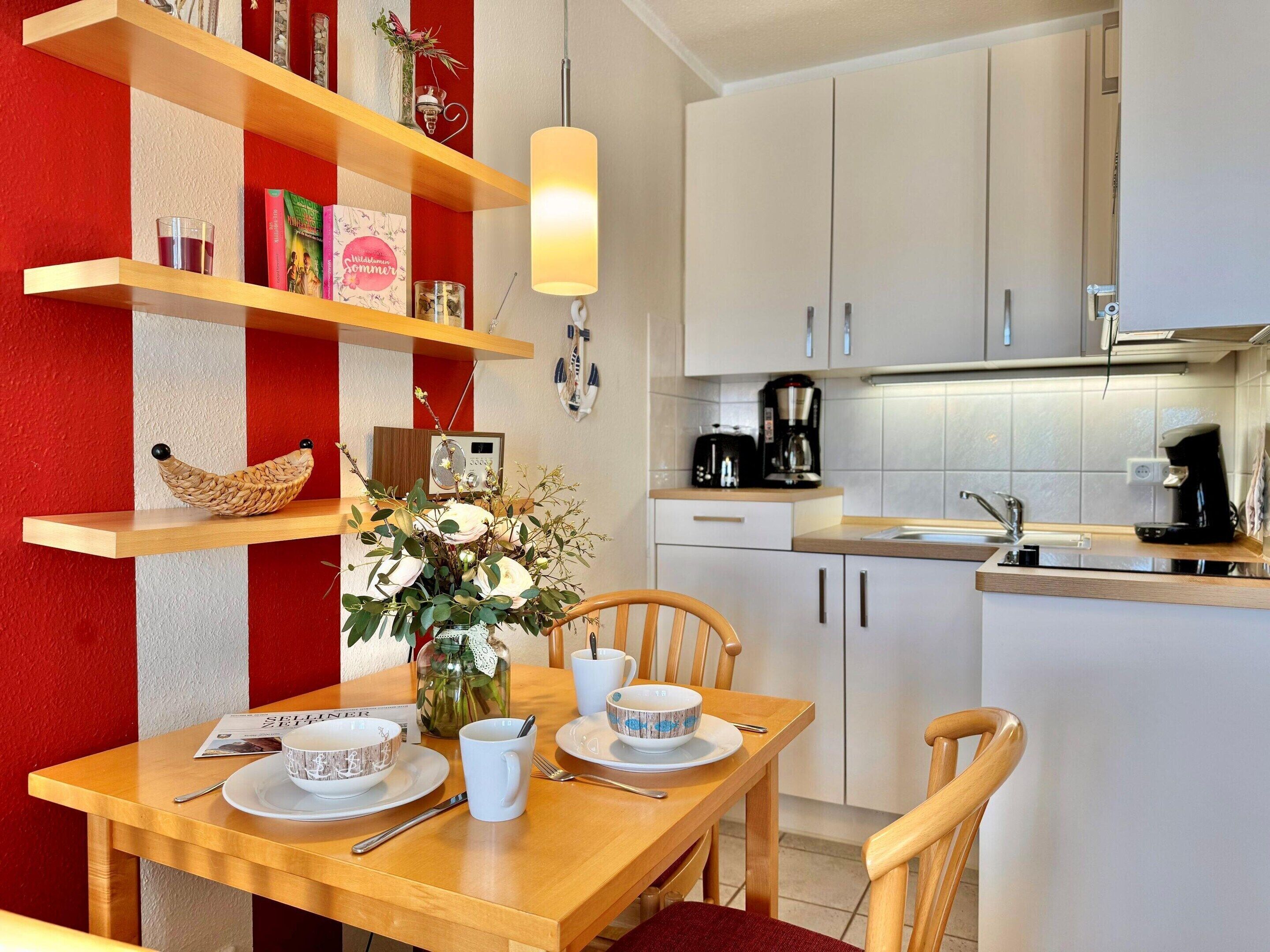 A modern kitchen with white cabinets, a wooden dining table with chairs, a coffee maker, and a radio.