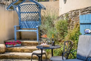 A patio with a blue chair, a round table with a bottle and glasses, and a small flower arrangement. - 3 Bed in Plymouth (oc-49520) (Newton Ferrers)