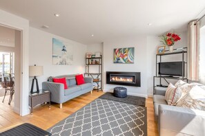 A modern living room with a fireplace, a sofa, a television, and a bookshelf. - 3 Bed in Plymouth (oc-49520) (Newton Ferrers)