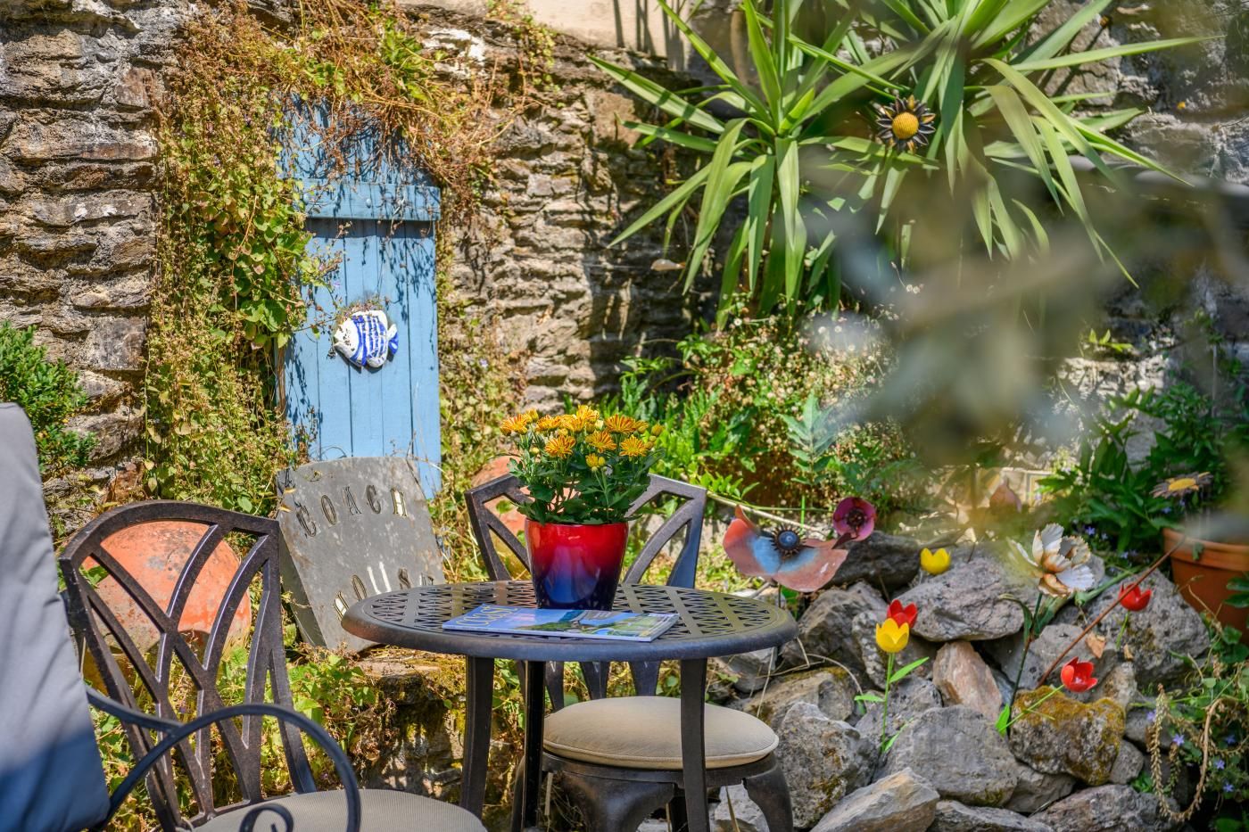 An outdoor seating area with a stone wall, a blue door, and a metal table with chairs.