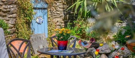 An outdoor seating area with a stone wall, a blue door, and a metal table with chairs.