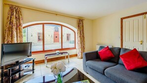 Ein Wohnzimmer mit Fernseher, Sofa, Couchtisch und Blick auf ein Gebäude durch große Fenster.