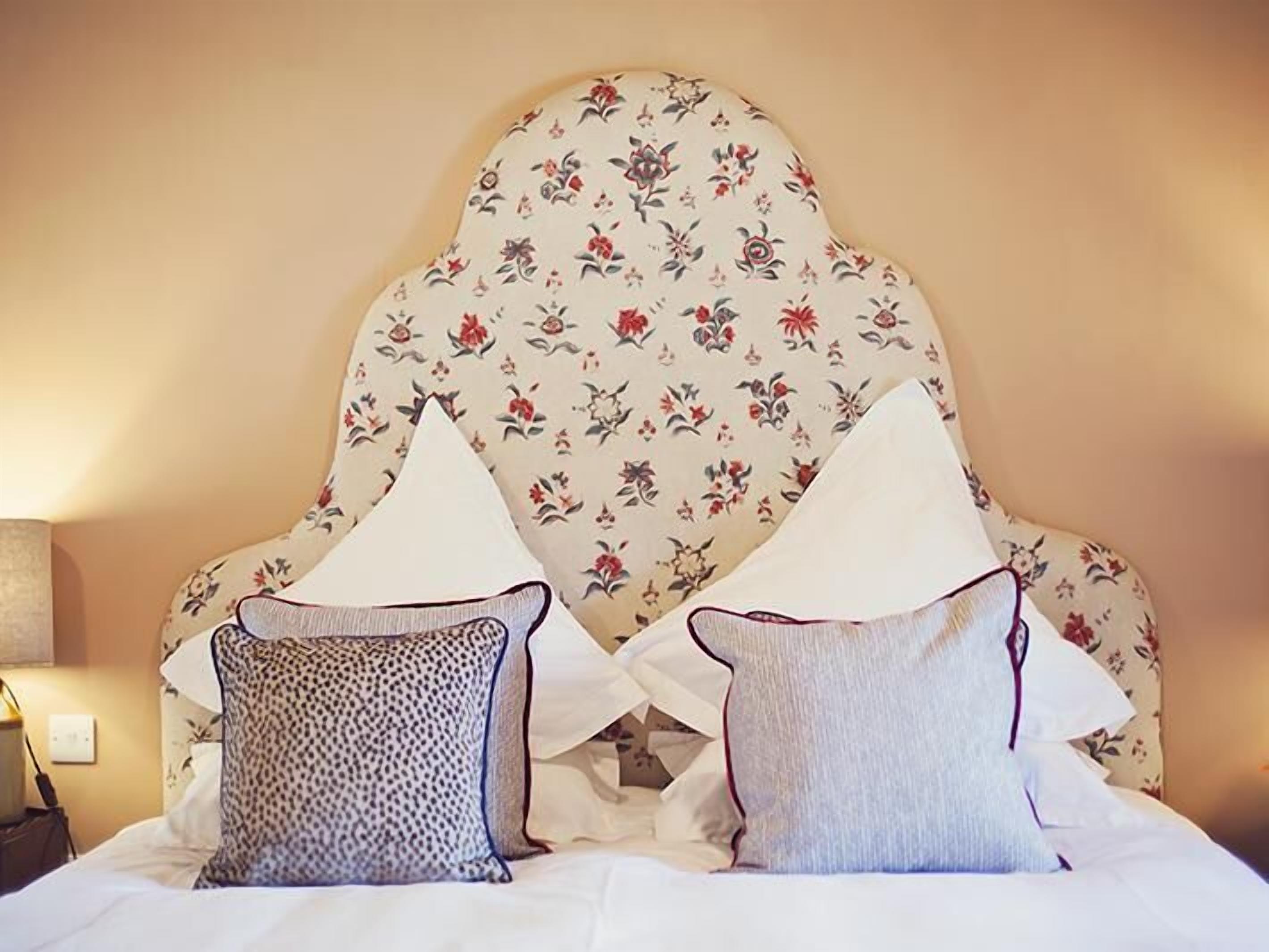 Una cama con dos almohadas, cabecera floral y una lámpara de noche.