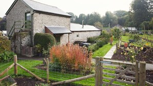 A stone building with a ramp, a garden with plants and a fence, and a pathway leading to another structure. - 1 Bed in Kington (oc-42939) (Huntington)