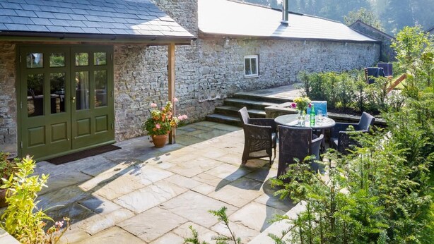 A stone house with a green door, a patio with outdoor furniture, and a small garden. - 1 Bed in Kington (oc-42939) (Huntington)