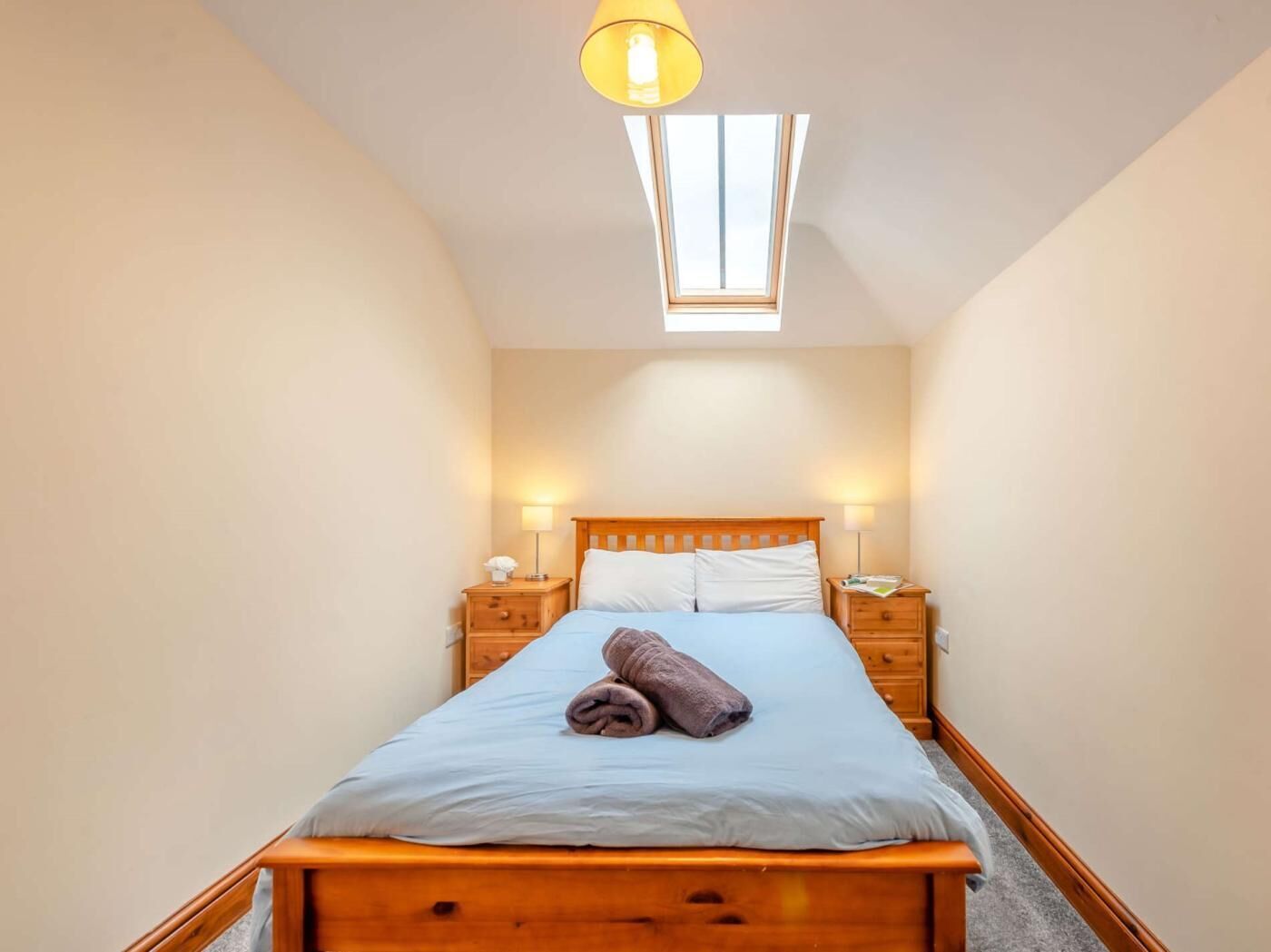 Un dormitorio con cama de madera, dos mesitas de noche, un tragaluz y una lámpara de noche.