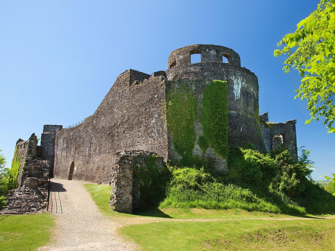 Un edifici de pedra històric amb una torre circular, envoltat de verdura i un cel serè.