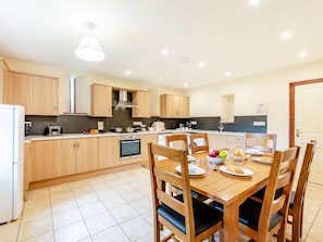A modern kitchen with wooden cabinets, a built-in oven, and a dining table set for four. - 3 Bed in Llandovery (oc-bn287) (Llanfair-ar-y-Bryn)