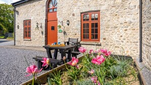 Ein Steinhaus mit roter Tür, Fenstern und einem Tisch mit Stühlen davor.