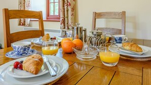 Ein Frühstückstisch mit Croissants, Obst, Orangensaft und einer Kaffeemaschine.