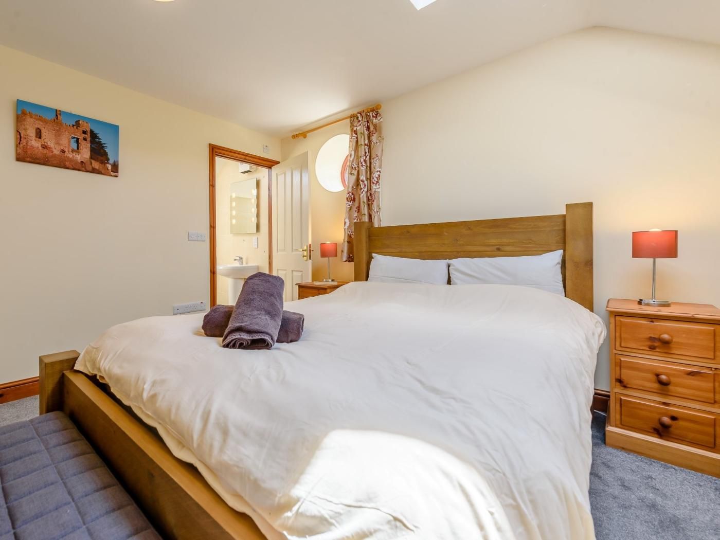 Ein Schlafzimmer mit einem großen Bett, einem Holzkopfteil, einem Nachttisch mit Lampe, einem Spiegel und einem Bild an der Wand.