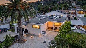 A modern residential building with a flat roof, a covered patio area, and a landscaped front yard with a palm tree. - Peaceful Tujunga Retreat Mountain Views Near Universal (Los Angeles)