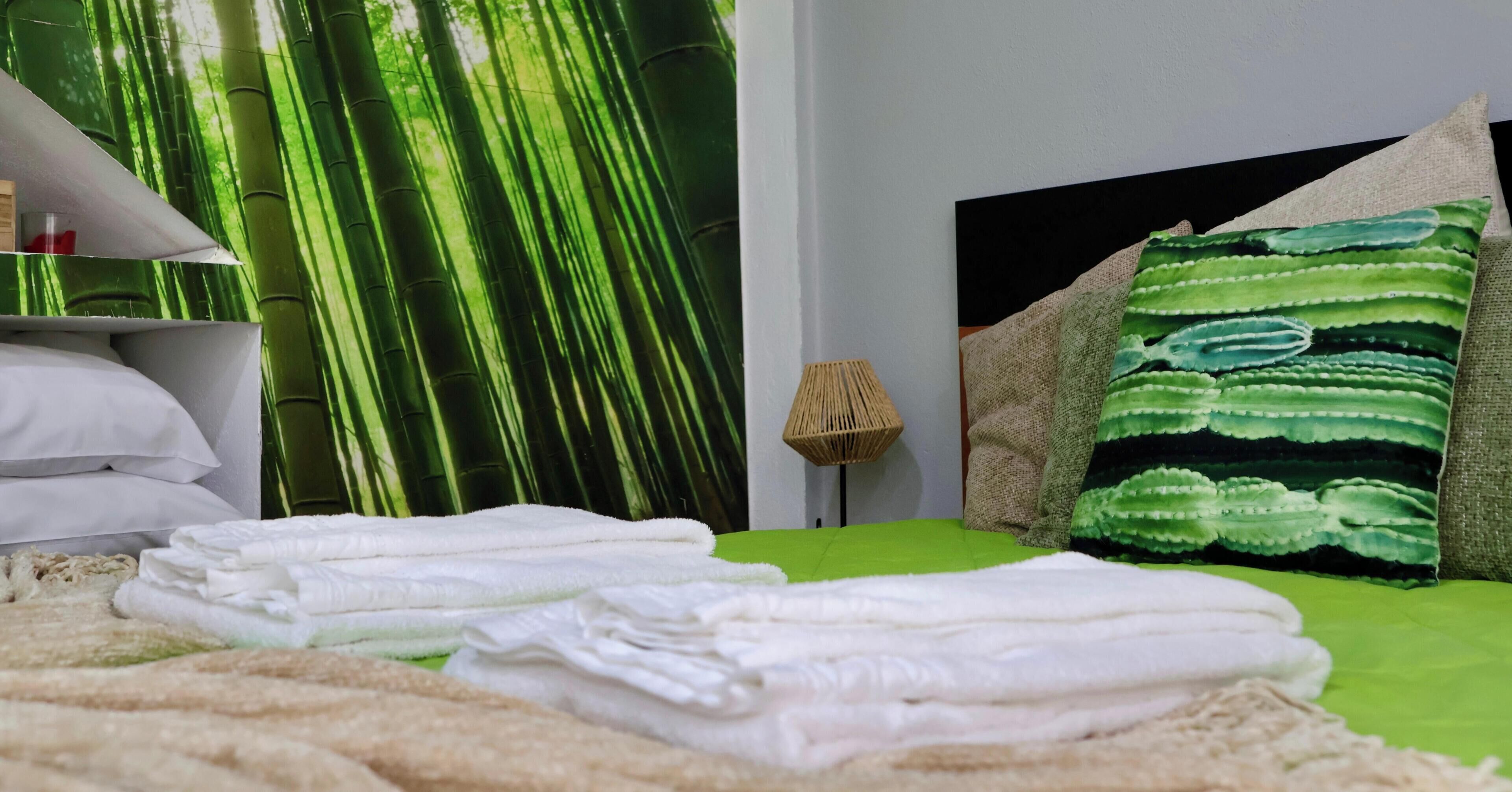 Una cama bien hecha con sábanas blancas, una colcha verde y una almohada verde y blanca a rayas.